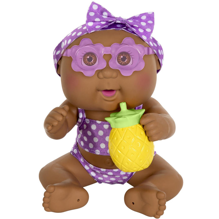 A 9-inch vinyl doll with a dark skin tone, wearing a purple swimsuit, sunglasses, and a purple polka-dotted headband, holding a pineapple-shaped bottle.