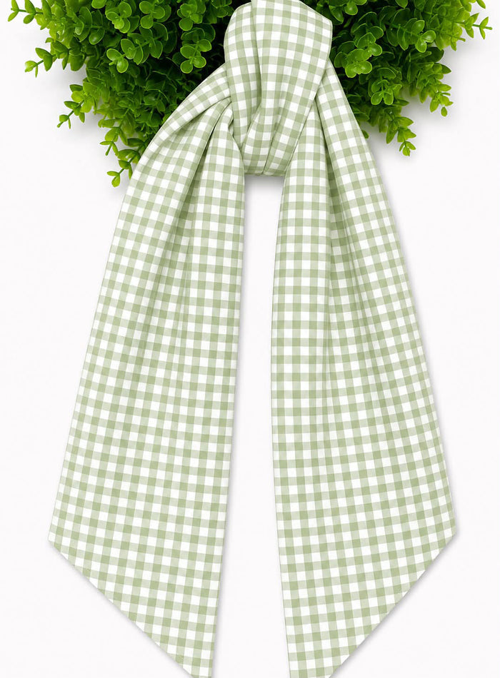 A light green and white gingham checkered sash, tied in a knot at the top and draped downward, set against a white background with green wreath at the top edge.