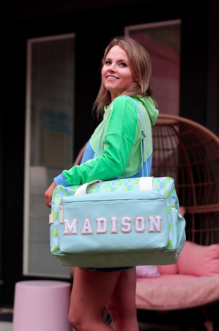 Woman holding a green bag with 'Madison' printed on it, standing on a patio.