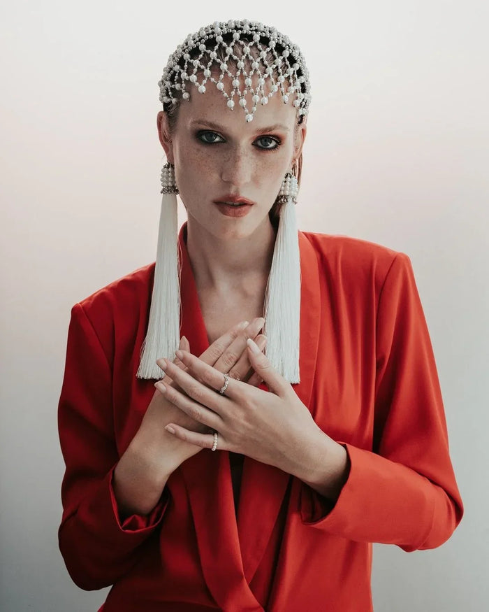 Woman wearing a red outfit with decorative headpiece and earrings against a plain background