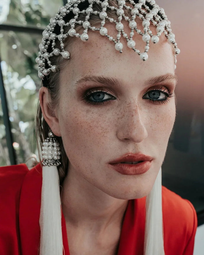 close up woman wearing a red outfit with decorative freja headbandand earrings against a plain background