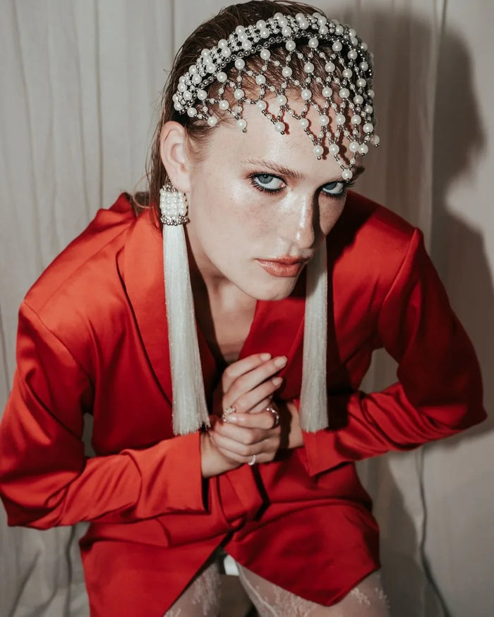 Woman wearing a red outfit with decorative headpiece and earrings against a plain background