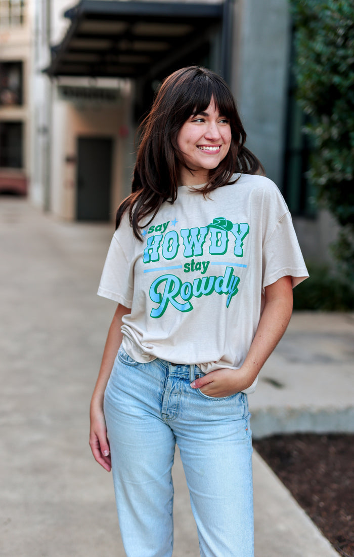 Woman wearing a white t-shirt with green text and light blue jeans standing outdoors.