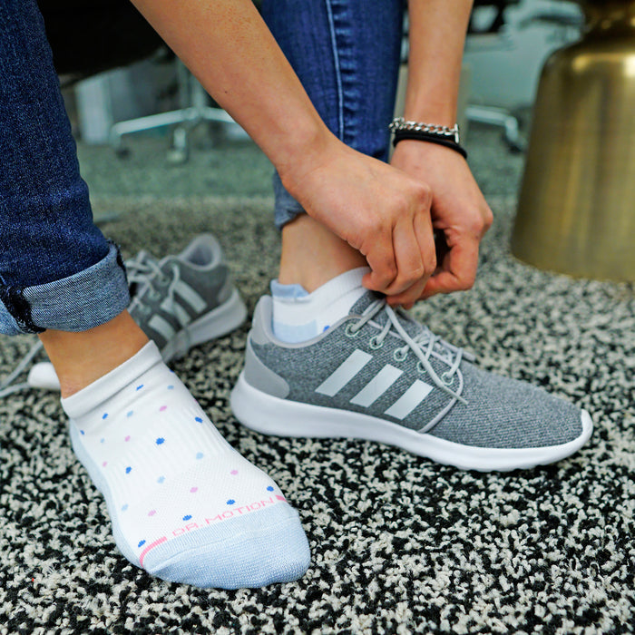Ankle compression sock with tri-color dots worn with a gray sneaker on a textured floor.